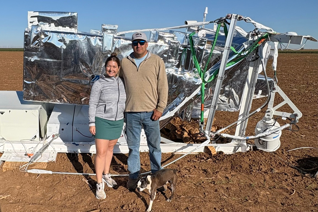 In this photo provided by Ann Walter, Ann Walter and her husband, Hayden, stand in front of a piece of NASA research equipment attached to a parachute that fell from the sky near their home in Edmonson, Texas, Thursday, Oct. 2, 2025. (Ann Walter via AP)