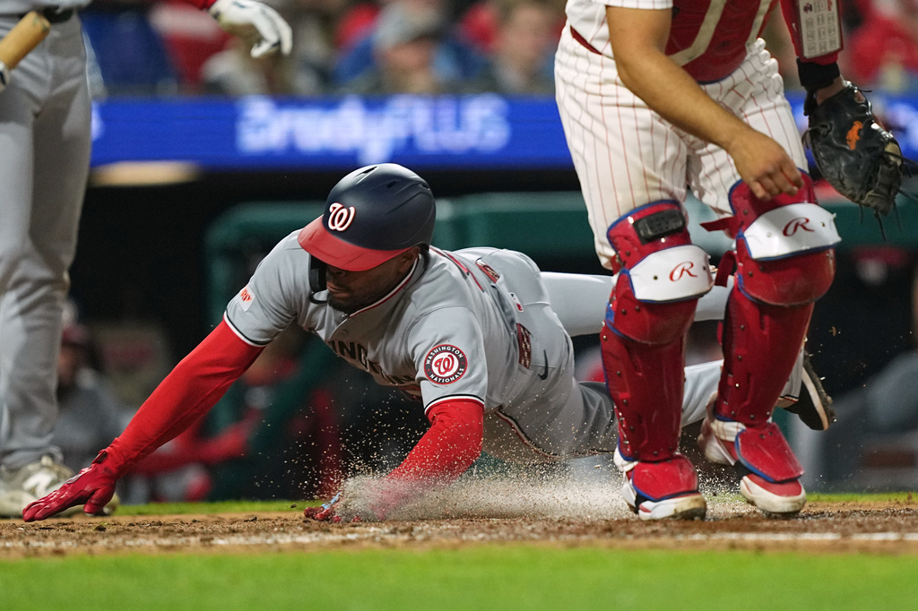 Washington Nationals' José Tena, center, scores past Philadelphia Phillies' Rafael Marchán, right, during the sixth inning of a baseball game, Monday, March 30, 2026, in Philadelphia. (AP Photo/Matt Rourke)