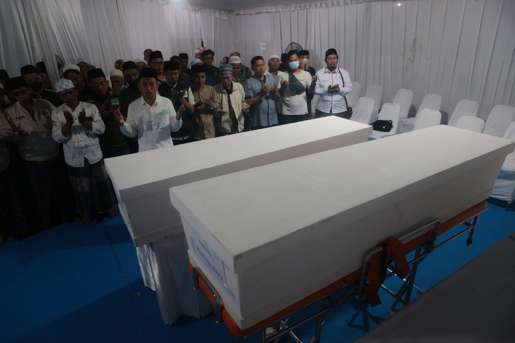 Men pray near the coffins containing the body of Nuruddin and Ahmad Rijalul Haq who are among the victims after a building under construction collapsed at an Islamic boarding school, during the handover of the bodies to the family members at the police hospital in Surabaya, East Java, Indonesia, Sunday, Oct. 5, 2025. (AP Photo/Trisnadi)
