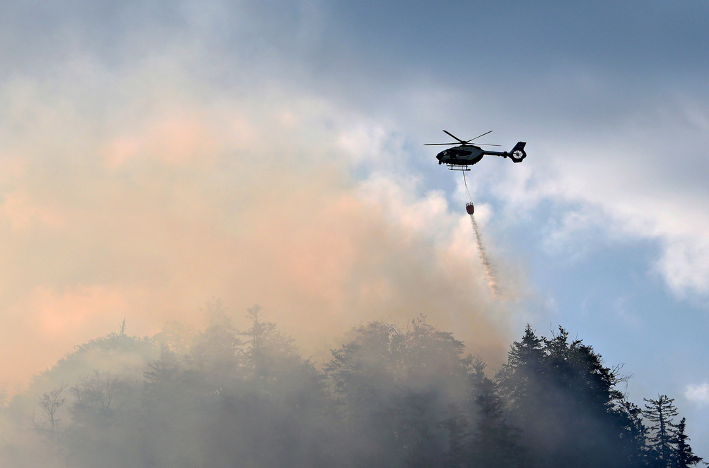 A helicopter drops water to extinguish a fire in the mountain forest in the Chiemgau Alps, near the village of Unterwossen, Germany, Thursday July 30, 2026. (Uwe Lein/dpa via AP)