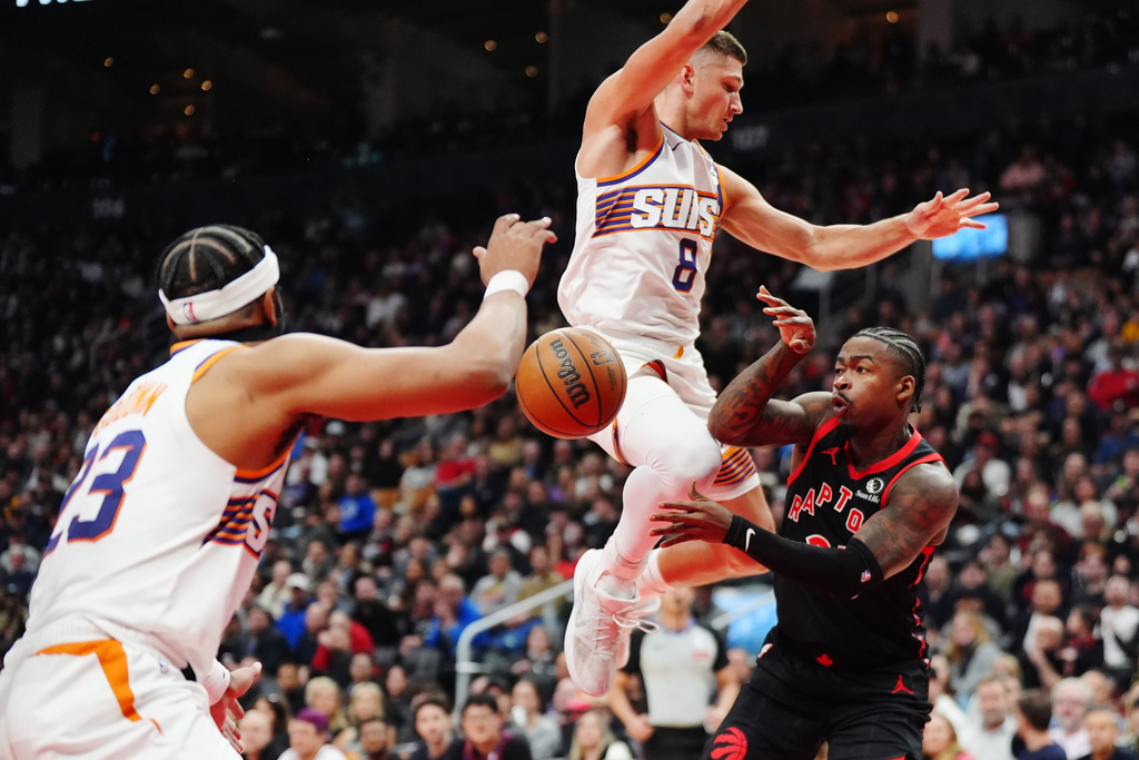 Toronto Raptors' Jamal Shead, right, passes the ball between Phoenix Suns' Jordan Goodwin, left, and Grayson Allen (8) during first-half NBA basketball game action in Toronto, Friday, March 13, 2026. (Frank Gunn/The Canadian Press via AP)