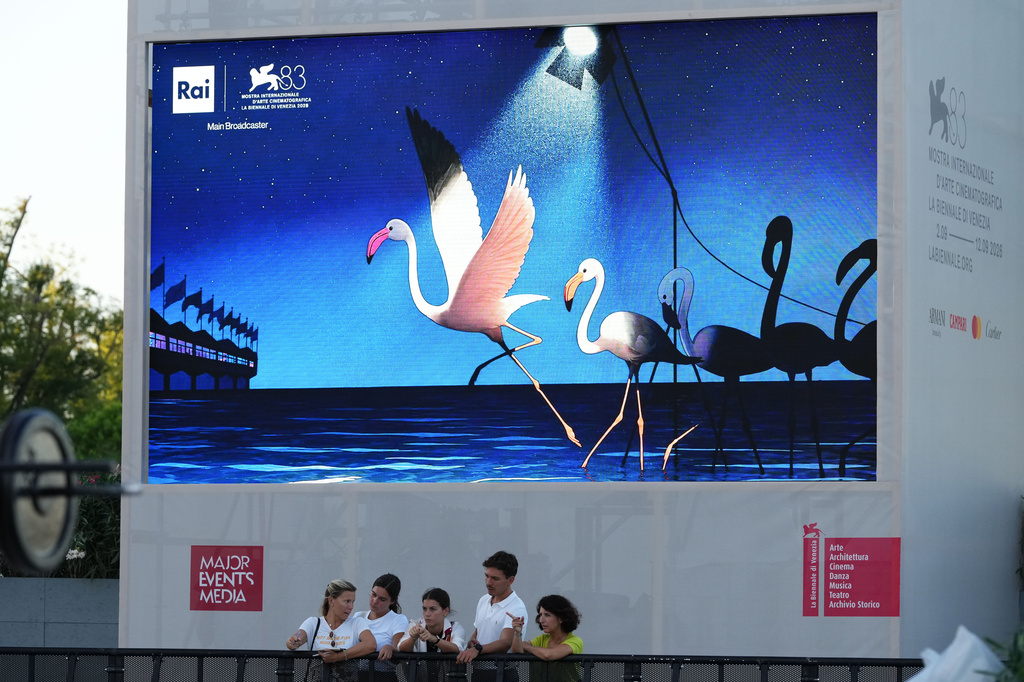 People gather in front of a billboard prior to the 83rd edition of the Venice Film Festival in Venice, Italy, on Monday, Aug. 31, 2026. (Photo by Alessandra Tarantino/Invision/AP)