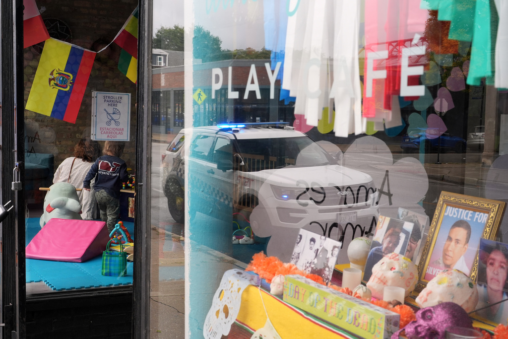 A Chicago Police Department car is reflected in the window of Luna y Cielo Play Cafe, where a framed picture is displayed of Silverio Villegas Gonzalez who was killed in an interaction with federal immigration enforcement (ICE) agents, as part of a Mexican Day of the Dead altar in Chicago's Logan Square neighborhood, Wednesday, Oct. 15, 2025. (AP Photo/Rebecca Blackwell)