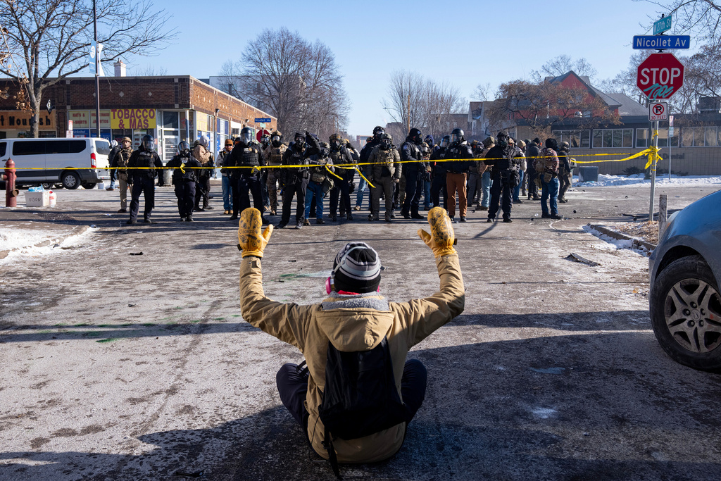 A protester sits on the street with his arms up in front of federal agents in Minneapolis, on Saturday, Jan. 24, 2026. (Alex Kormann/Star Tribune via AP)