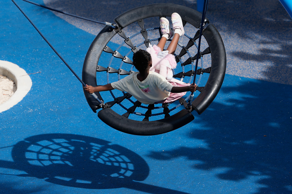 A girl swings at a playscape at DC Alexander Park, a former parking lot that was transformed into a public space that doubles as flood infrastructure, Tuesday, June 30, 2026, in Fort Lauderdale, Fla. (AP Photo/Lynne Sladky)