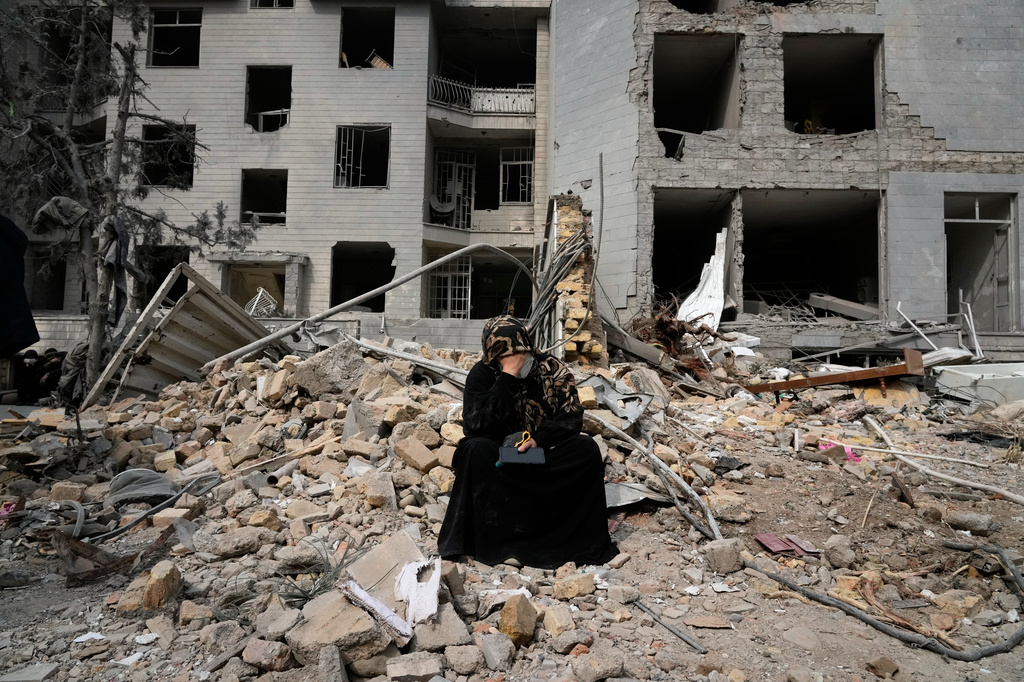 FILE - A woman sits on rubble across from a residential building damaged last Sunday during the U.S.-Israeli air campaign in Tehran, Iran, March 12, 2026. (AP Photo/Vahid Salemi, File)