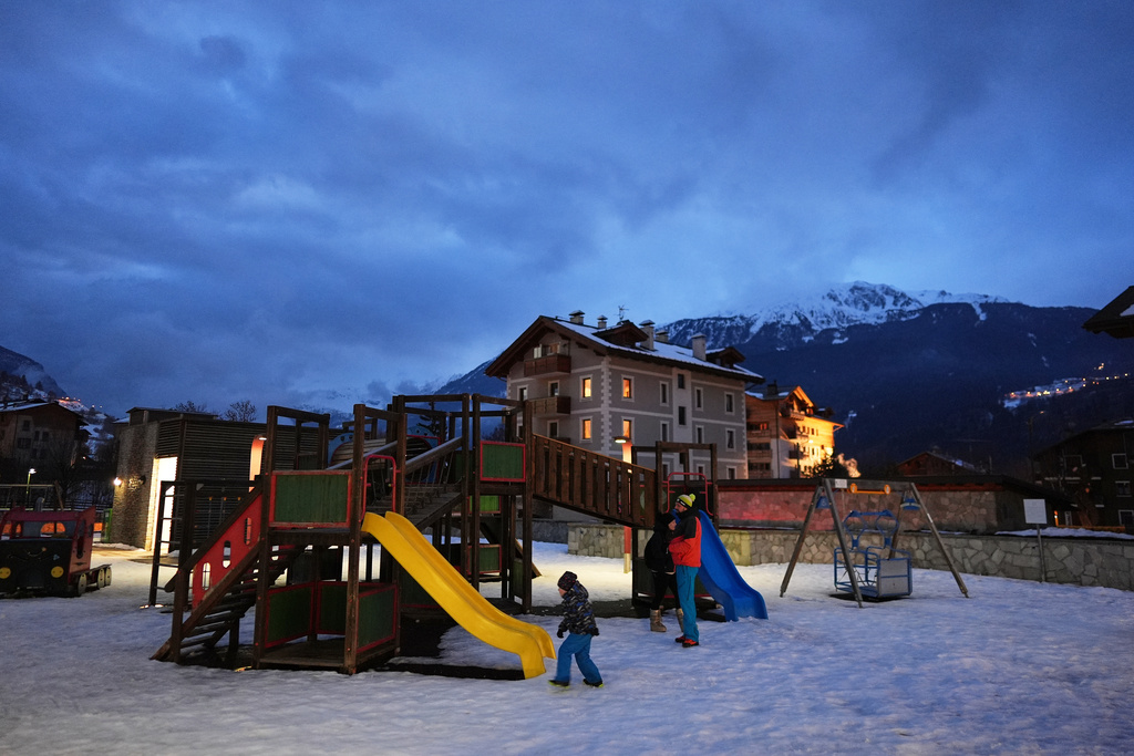 A family visiting for the 2026 Winter Olympics plays on a playground in the snow as night falls, in Bormio, Italy, Tuesday, Feb. 10, 2026. (AP Photo/Rebecca Blackwell)
