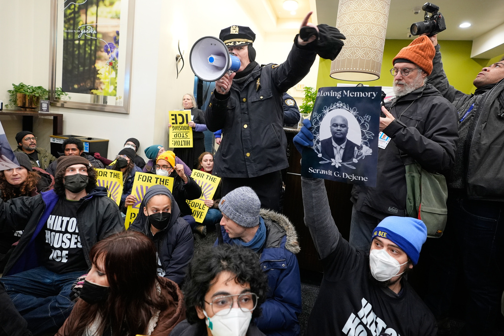 A police officer, top, makes an announcement about impending arrests during a sit-in in the lobby of a Hilton Garden Inn in New York, Tuesday, Jan. 27, 2026. (AP Photo/Seth Wenig)