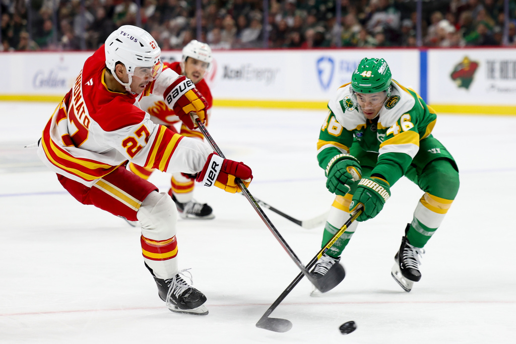 Calgary Flames right wing Matt Coronato (27) shoots on goal as Minnesota Wild defenseman Jared Spurgeon (46) defends during the second period of an NHL hockey game Sunday, Nov. 9, 2025, in St. Paul, Minn. (AP Photo/Ellen Schmidt)