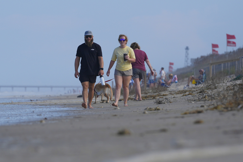 People walk along the beach as waves as red flags, indicating swimming is prohibited, are raised at the beach in Duck, N.C., Tuesday, Aug. 19, 2025, as precautions are taken ahead of Hurricane Erin. (AP Photo/Pablo Martinez Monsivais)