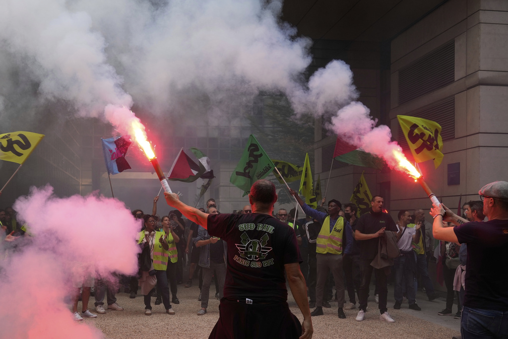 Striking rail workers wave flares into the Paris headquarters of the Economics Ministry during a protest called by major trade unions to oppose budget cuts, in Paris, France, Thursday, Sept. 18, 2025. (AP Photo/Michel Euler)