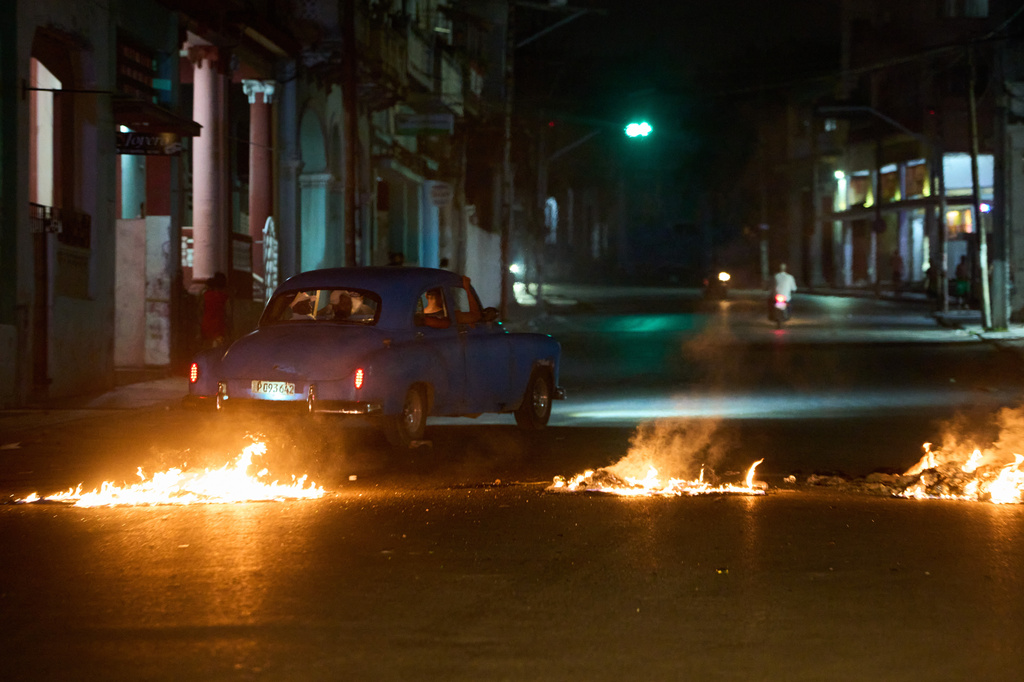 People drive a classic American car through a barricade set up by residents protesting against prolonged power outages in Havana, Cuba, Wednesday, May 13, 2026. (AP Photo/Ramon Espinosa)