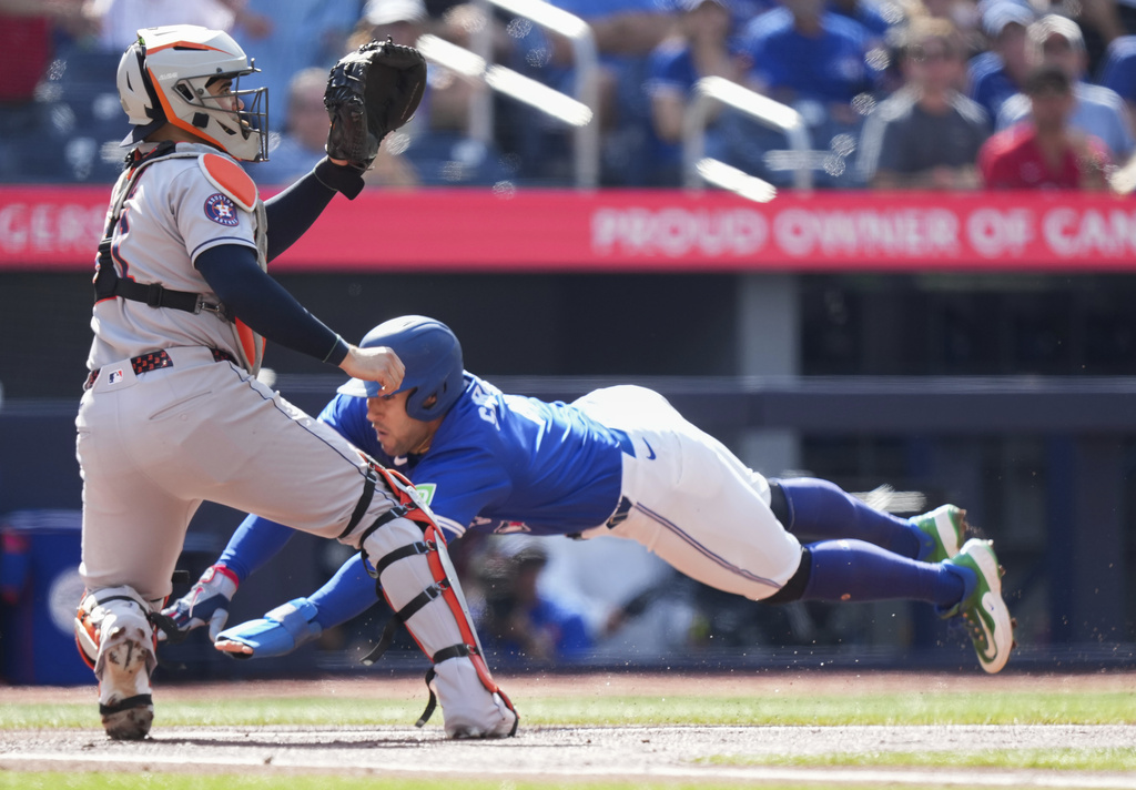 Toronto Blue Jays designated hitter George Springer dives past Houston Astros catcher Yainer Diaz to score a run during the first inning of a baseball game in Toronto, Thursday, Sept. 11, 2025. (Nathan Denette/The Canadian Press via AP)
