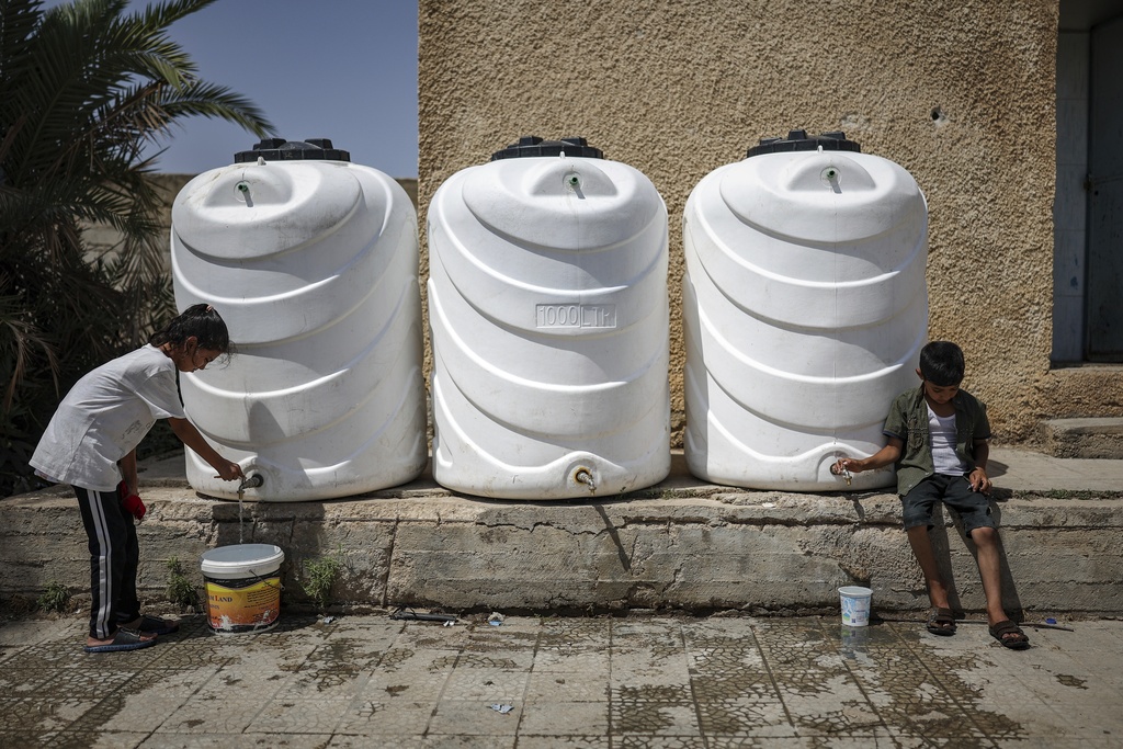 Children collect water from containers at a school sheltering displaced Syrian Bedouins from the Sweida region, forced from their homes after clashes between Druze militias and Bedouin groups, in the village of Abtaa in rural Daraa, Syria, Aug. 15, 2025. (AP Photo/Ghaith Alsayed)