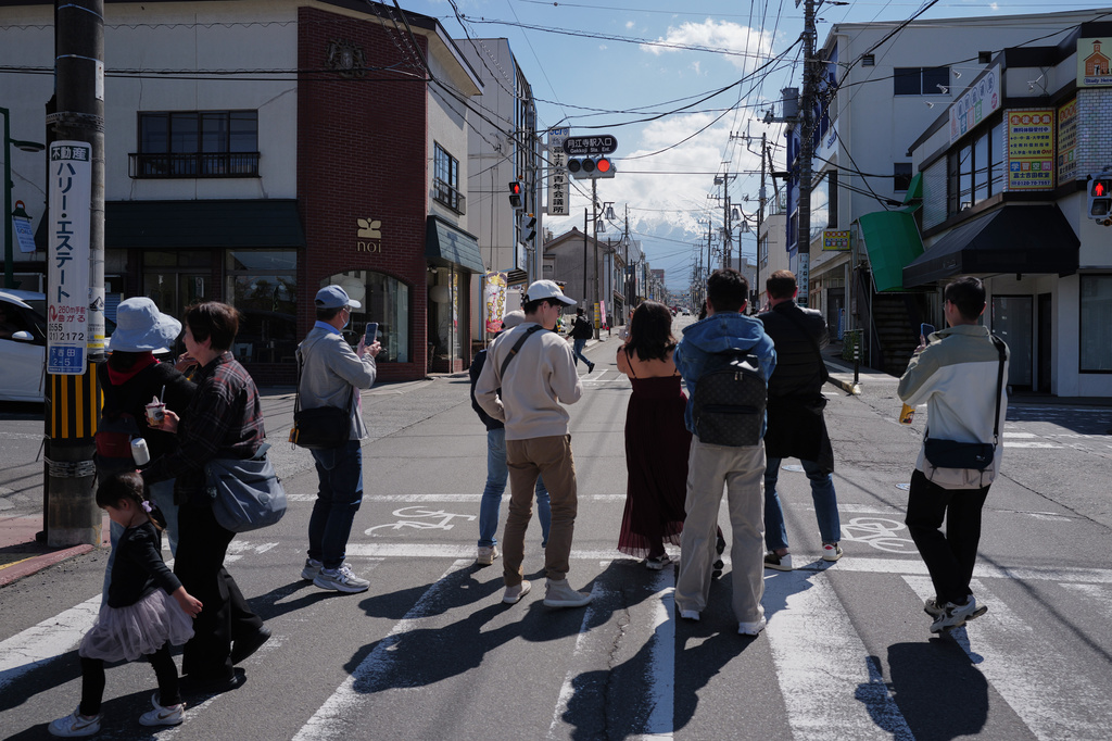 Foreign visitors stand to photograph Mount Fuji though Honcho Street on Wednesday, April 8, 2026, in Fujiyoshida, west of Tokyo. (AP Photo/Eugene Hoshiko)