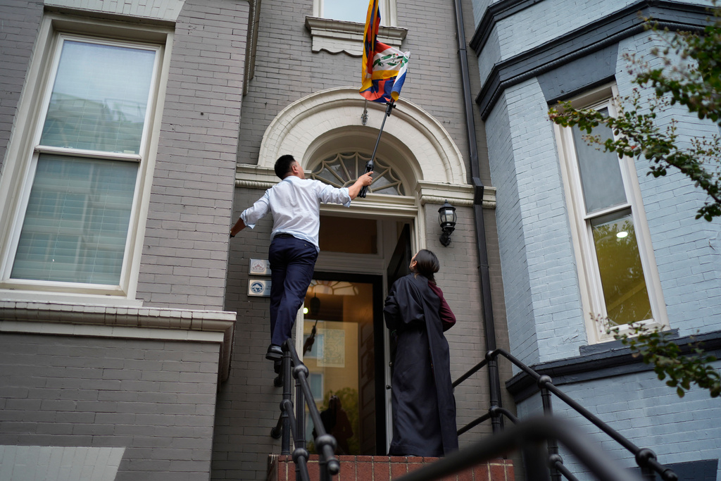 Namkyi, right, a Tibetan former political prisoner who was arrested at 15 for protesting Chinese rule, watches as Tsultrim Gyatso, China Director at Office of Tibet, untangles the Tibetan flag over the office entrance in Washington, Oct. 9, 2025. (AP Photo/David Goldman)
