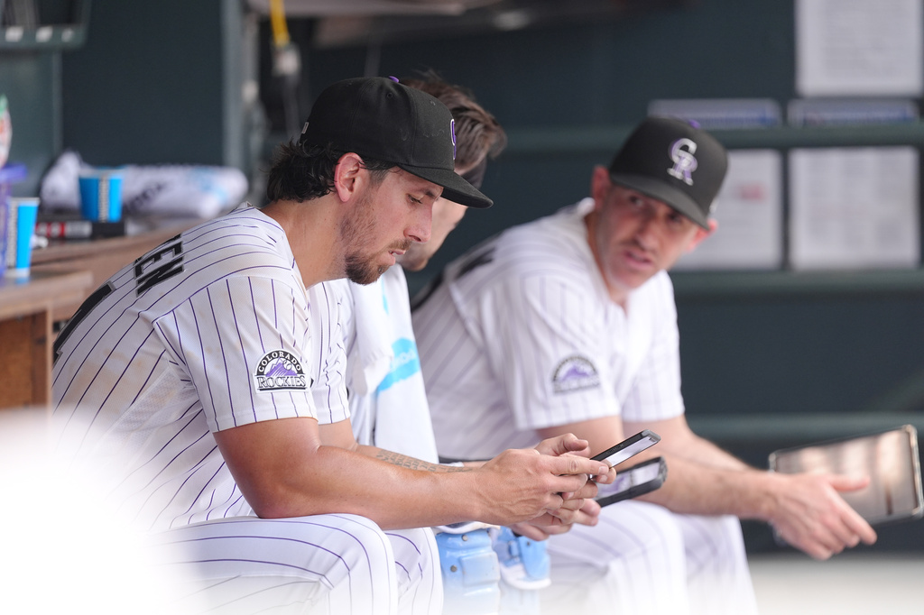 Colorado Rockies starting pitcher Michael Lorenzen, left, looks at a tablet as catcher Brett Sullivan, center, confers with pitching coach Alon Leichman, right, in the dugout in the fourth inning of a baseball game against the Pittsburgh Pirates, Sunday, June 21, 2026, in Denver. (AP Photo/David Zalubowski)
