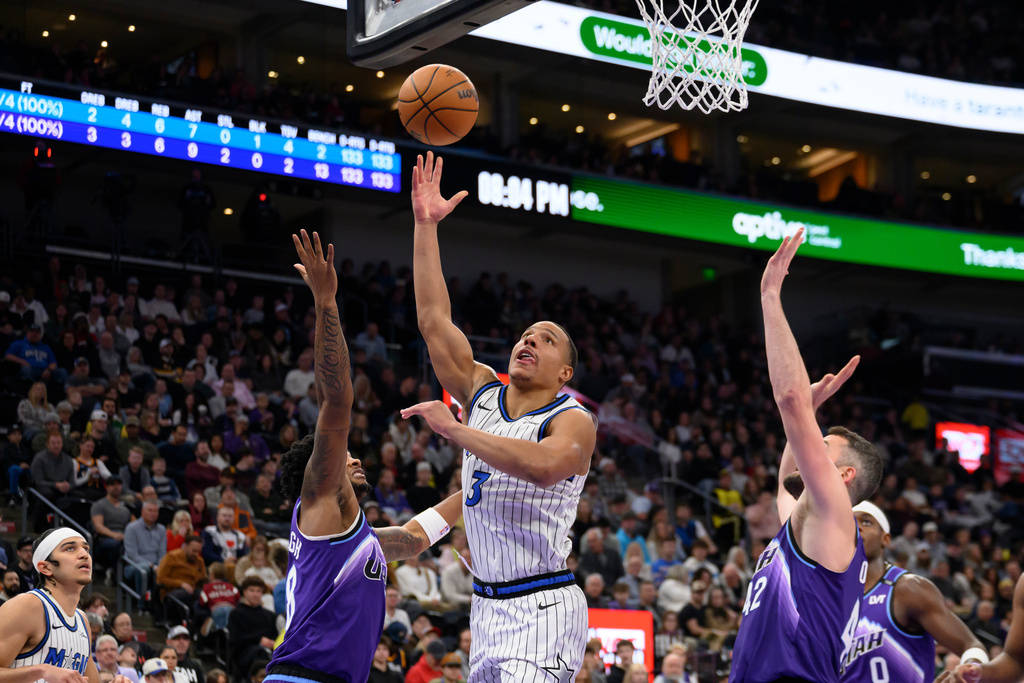 Orlando Magic guard Desmond Bane, center, lays up the ball to the basket over Utah Jazz forward Brice Sensabaugh, center left, during the first half of an NBA basketball game, Saturday, Dec. 20, 2025, in Salt Lake City. (AP Photo/Tyler Tate)