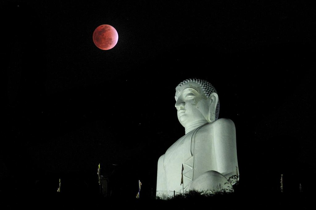 FILE - A lunar eclipse in the night sky behind a statue of the Buddha in Kurunegala, Sri Lanka, Saturday, Dec. 10, 2011. (AP Photo/ Eranga Jayawardena, File)