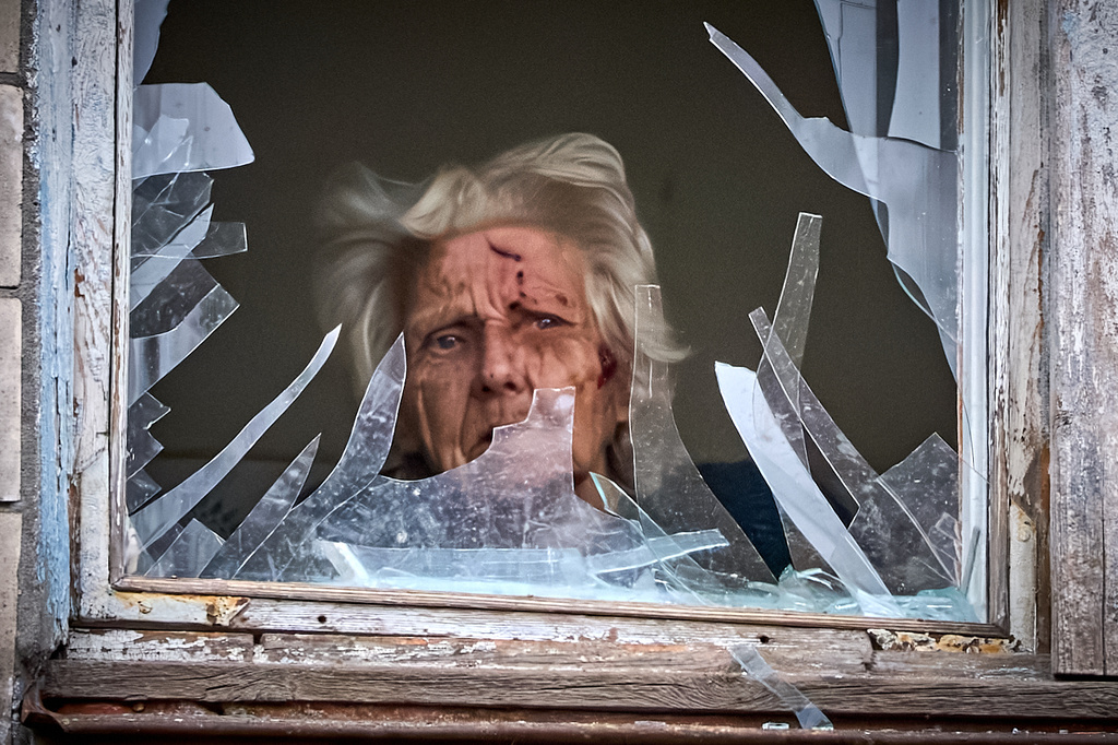 An injured elderly woman looks out of her broken window as an apartment building was hit by a Russian drone during an aerial attack in Kyiv, Ukraine, Tuesday, Dec. 23, 2025. (AP Photo/Efrem Lukatsky)