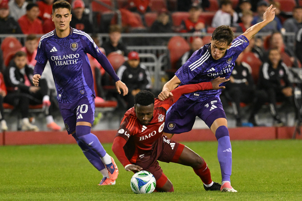 Toronto FC's Derrick Etienne Jr., centre, is tackled by Orlando City SC's Rodrigo Brekalo, right, during first half MLS soccer action in Toronto on Saturday, Oct. 18, 2025. (Jon Blacker/The Canadian Press via AP)