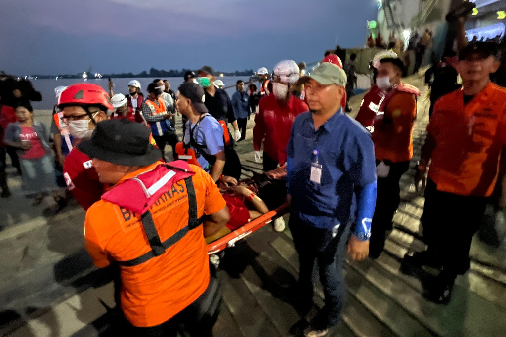 In this photo taken with a smartphone, rescuers carry a survivor on a stretcher after a ferry sank in bad weather in the Java Sea, upon arrival at a port in Banjarmasin, South Kalimantan, Indonesia, Sunday, Sept. 13, 2026. (AP Photo/Iman Satria)