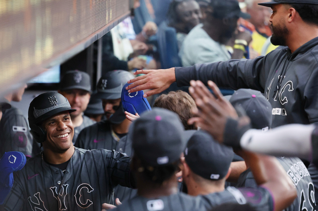 New York Mets' Juan Soto, left, high-fives teammates in the dugout after scoring during the seventh inning of a baseball game against the Philadelphia Phillies, Saturday, June 27, 2026, in New York. (AP Photo/Heather Khalifa)