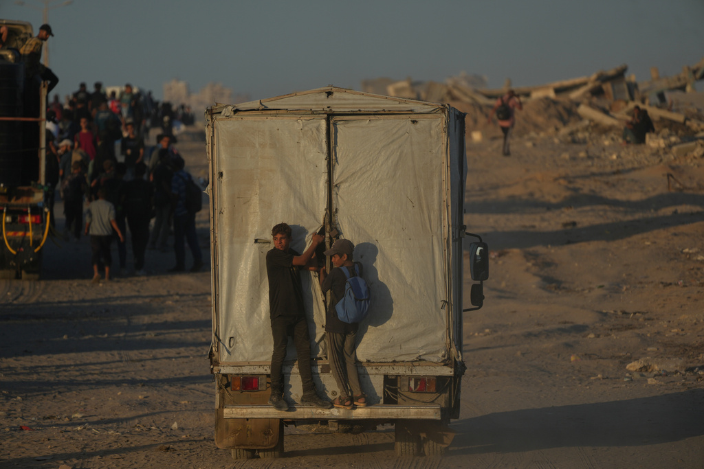 Displaced Palestinians cling to the back of a truck loaded with belongings as it drives along the coastal road near Wadi Gaza in the central Gaza Strip, heading toward Gaza City, Friday, Oct. 10, 2025, after Israel and Hamas agreed to a pause in their war and the release of the remaining hostages. (AP Photo/Abdel Kareem Hana)