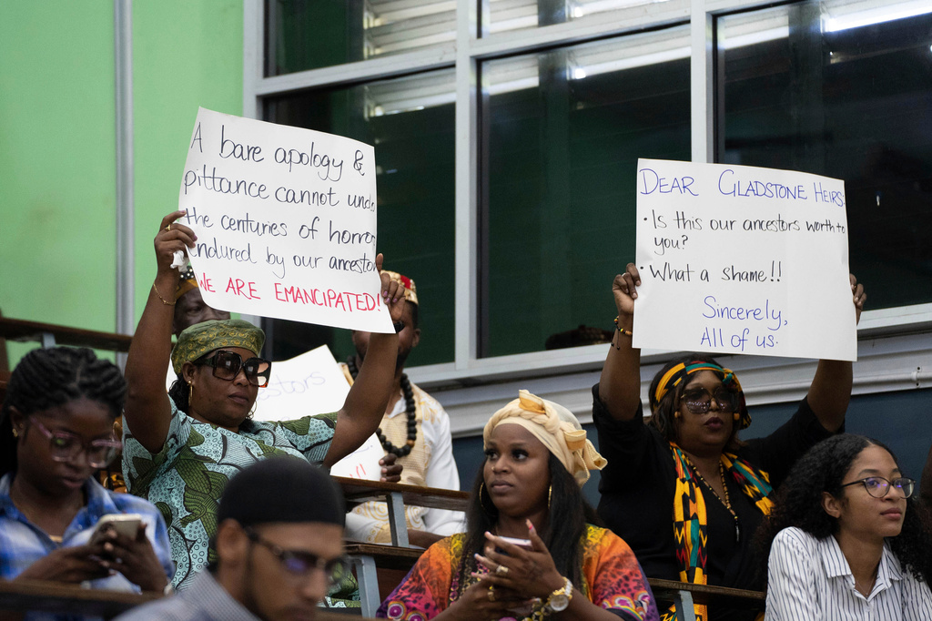 FILE - People hold signs during a speech by Charles Gladstone, a descendant of former plantation owner John Gladstone, as he delivers an apology on behalf of the Gladstone family at Georgetown University in Georgetown, Guyana, Friday, Aug. 25, 2023. (AP Photo/Chris Leung, File)