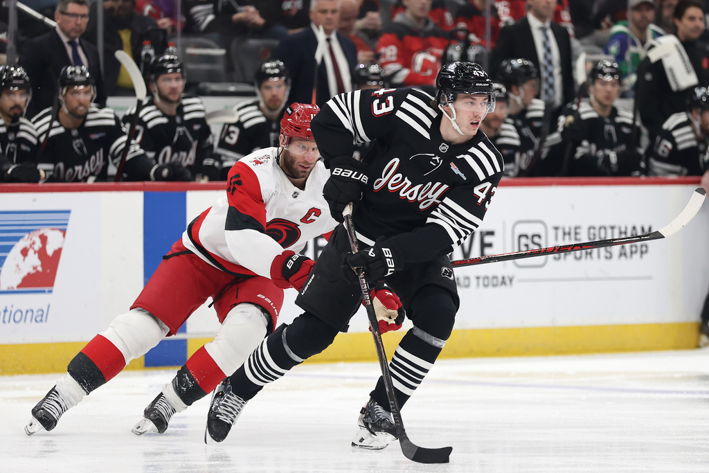 New Jersey Devils defenseman Luke Hughes (43) skates with the puck past Carolina Hurricanes center Jordan Staal (11) during the first period of an NHL hockey game Saturday, Jan. 17, 2026, in Newark, N.J. (AP Photo/Adam Hunger)