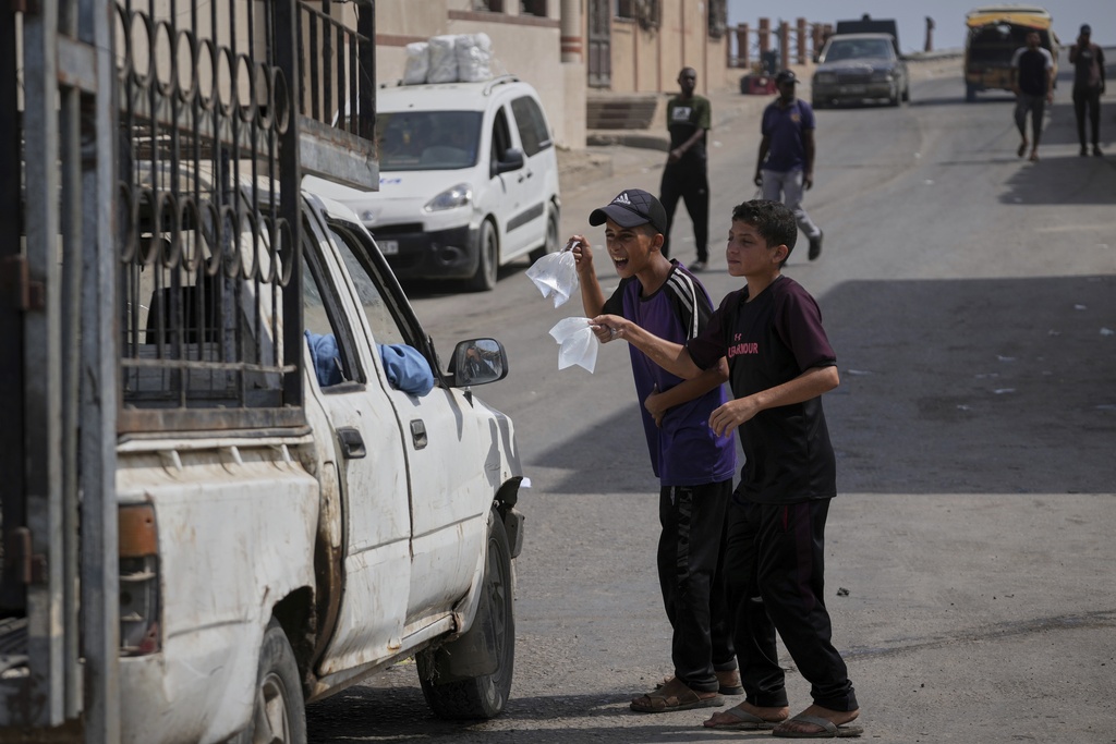 Palestinian children sell bags of drinking water during a hot summer day with temperatures reaching 36 °C (97 °F) in Deir al-Balah, central Gaza Strip, Wednesday, Aug, 13, 2025. (AP Photo/Abdel Kareem Hana)