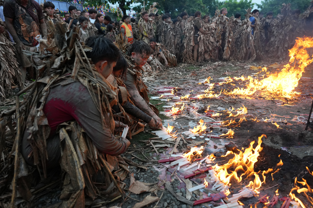 Catholic devotees covered in mud and dried banana leaves light candles as they participate at the mud people festival on the feast day of Saint John the Baptist at Bibiclat, Nueva Ecija province, northern Philippines on Wednesday, June 24, 2026. (AP Photo/Aaron Favila)
