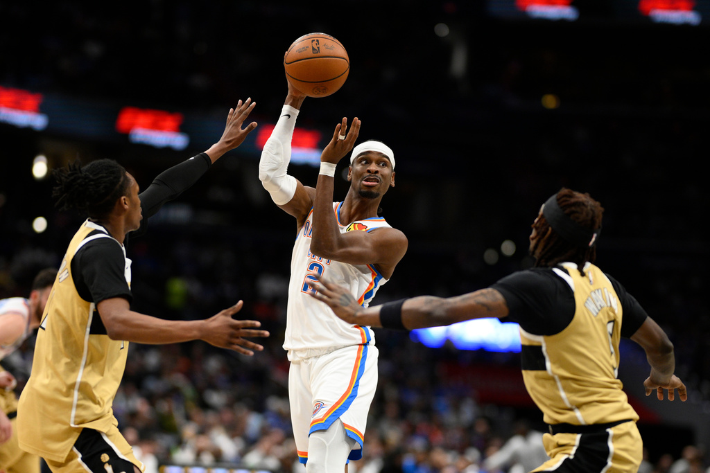 Oklahoma City Thunder guard Shai Gilgeous-Alexander (2) looks to pass the ball against Washington Wizards guards Jamir Watkins, right, and Bub Carrington, left, during the first half of an NBA basketball game, Saturday, March 21, 2026, in Washington. (AP Photo/Nick Wass)