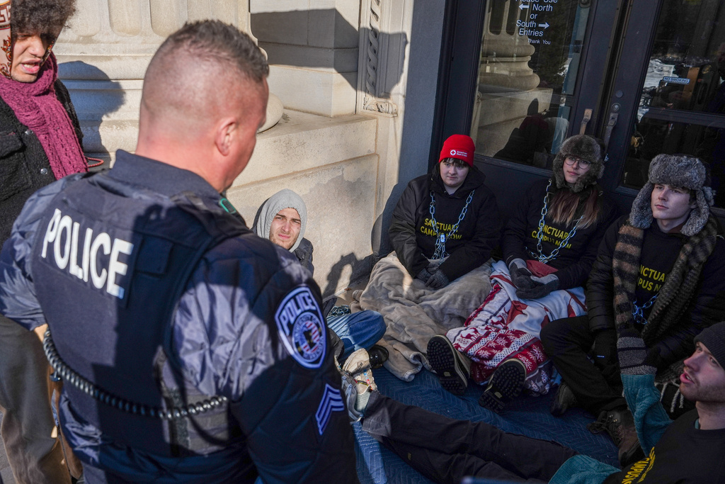 A University of Minnesota Police officer threatens student protesters with arrest for chaining themselves to a door on campus during an anti-ICE protest, on Friday, Feb. 6, 2026, in Minneapolis. (AP Photo/Ryan Murphy)