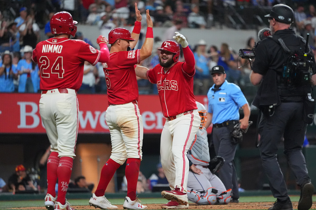 Texas Rangers Jake Burger, right, celebrates his home run scoring teammates Brandon Nimmo (24) and Josh Jung during the 8th inning of a baseball game against the Houston Astros, Friday, July 10, 2026, in Arlington, Texas. (AP Photo/LM Otero)