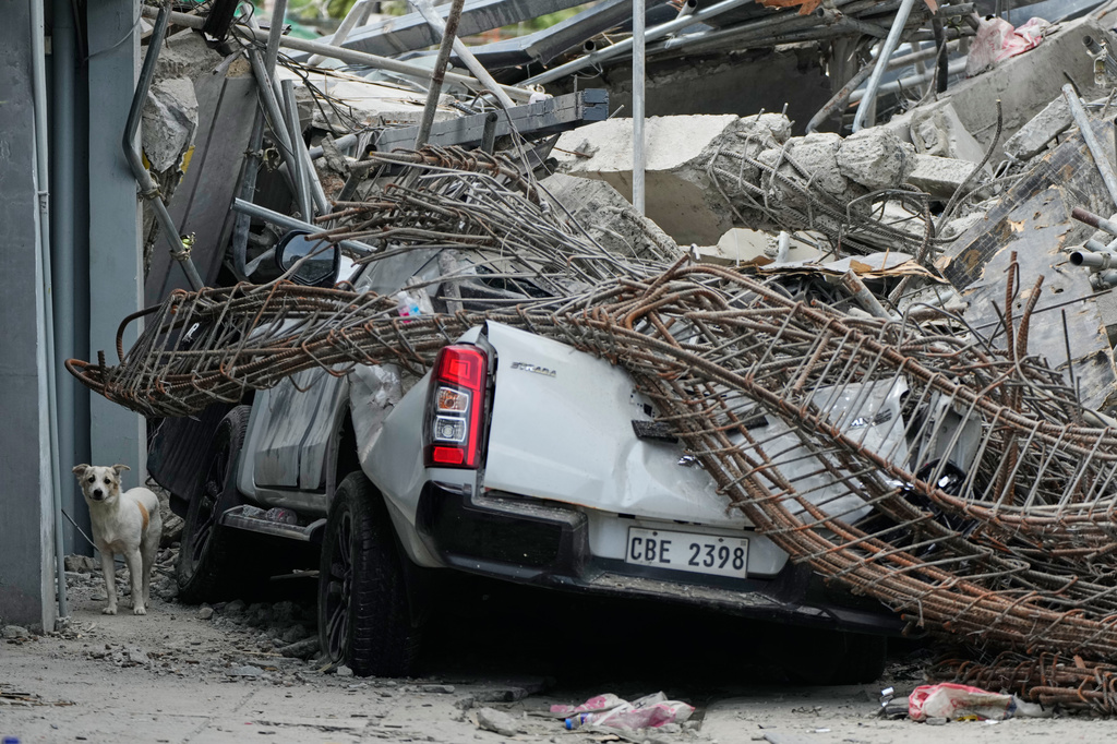 A dog stands beside a damaged pick-up truck at the ruins of a collapsed building where multiple people are believed to be trapped in Angeles city in Pampanga province, north of Manila, Philippines, Monday, May 25, 2026. (AP Photo/Aaron Favila)