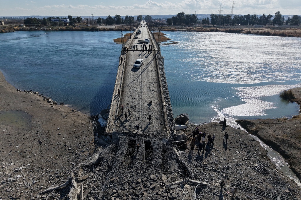 People cross the damaged Al-Rashid Bridge on foot, destroyed by retreating Syrian Democratic Forces (SDF) troops, a day after Syrian government troops took control of the area on the outskirts of Raqqa, northeastern Syria, Monday, Jan. 19, 2026. (AP Photo/Omar Albam)