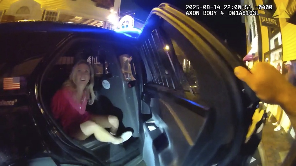 In an image taken from police body camera footage, a Newport Police officer closes the door of a cruiser with the detained Rhode Island Special Assistant Attorney General Devon Flanagan after an encounter that ended with officers detaining Flanagan on trespassing charges, Aug. 14, 2025, in Newport, R.I. (Newport Police Department via AP)