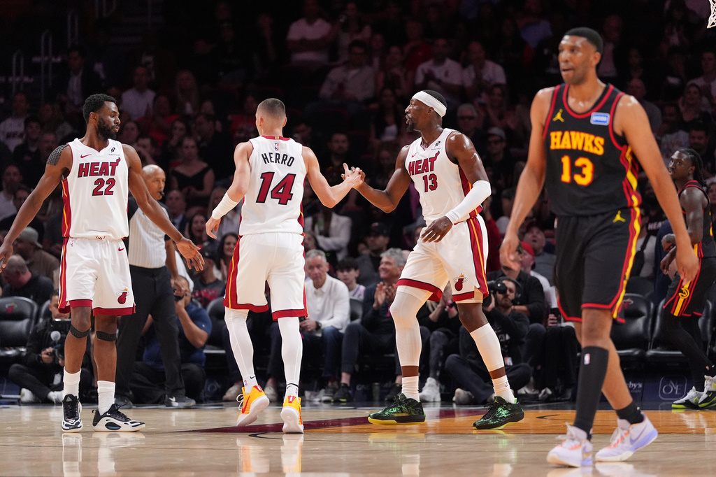 Miami Heat center Bam Adebayo, center right, celebrates with guard Tyler Herro (14) and forward Andrew Wiggins (22) as Atlanta Hawks center Tony Bradley, right, walks downcourt during the first half of an NBA basketball game, Sunday, April 12, 2026, in Miami. (AP Photo/Rebecca Blackwell)