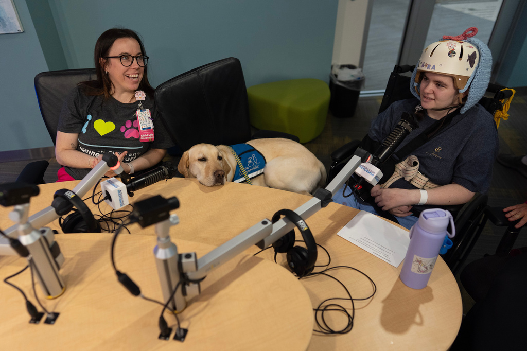Cincinnati Children's Hospital Child Life Specialist Maggie O'Grady, left, and facility dog Grover, center, work with patient Kira Hodge at the hospital's Seacrest Studios to produce a closed-circuit television show beamed into patient rooms, at Cincinnati Children's Hospital in Cincinnati, Monday, May 4, 2026. (AP Photo/Carolyn Kaster)
