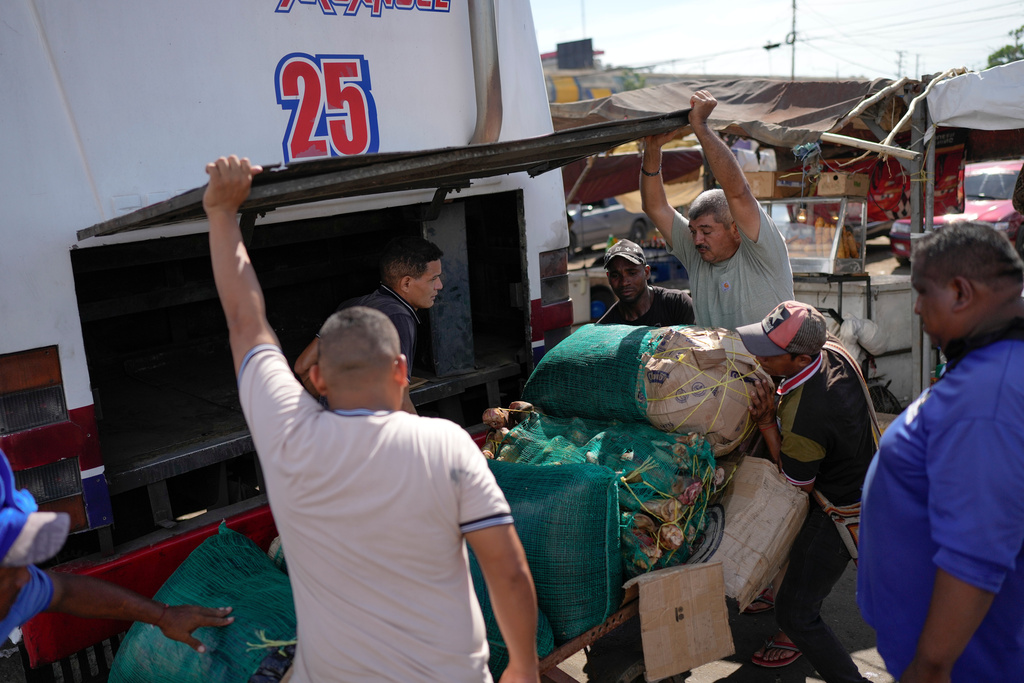 Butcher Richard Lazcano, top right, waits to load sacks of meat he purchased onto a bus to take to the Colombian border to sell, at Las Pulgas market in Maracaibo, Venezuela, Thursday, June 19, 2025. Lazcano returned to his old job after his attempt to reach the United States was cut short when the Trump administration suspended asylum appointments. (AP Photo/Matias Delacroix)
