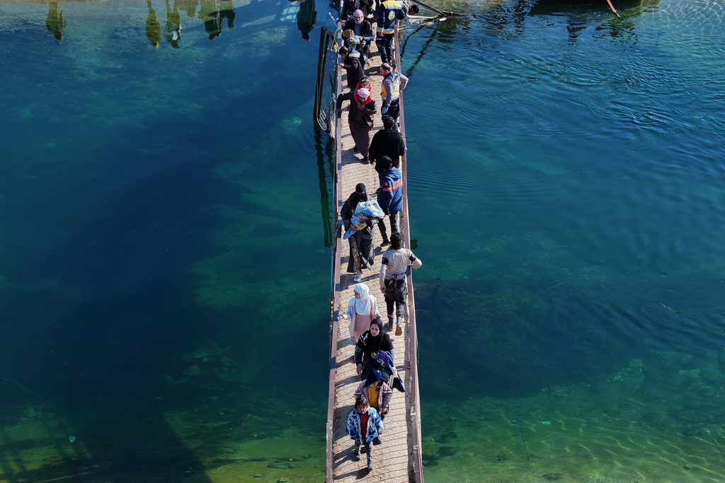 Displaced Syrians walk to cross at a river crossing near the village of Rasm al-Harmil al-Imam in the eastern Aleppo countryside, near the front line with the Kurdish-led Syrian Democratic Forces, in Deir Hafer, Syria, Friday, Jan. 16, 2026. (AP Photo/Ghaith Alsayed)