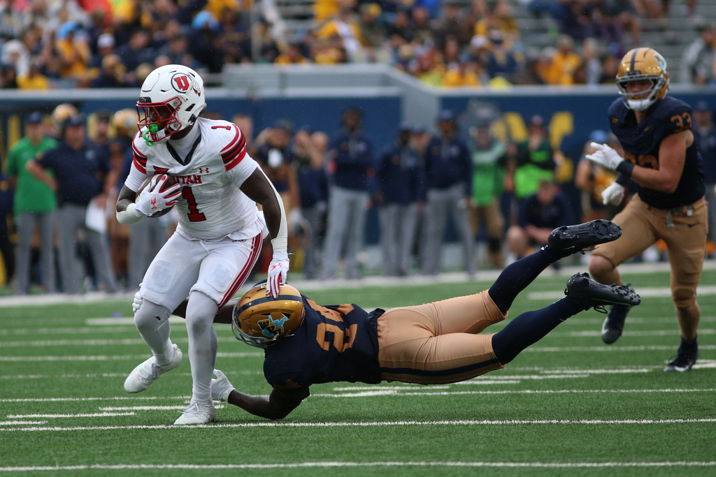 Utah running back Wayshawn Parker (1) slips the tackle by West Virginia safety Darrian Lewis (24) during the second half of an NCAA college football game, Saturday, Sept, 27, 2025, in Morgantown, W.Va. (AP Photo/ William Wotring)