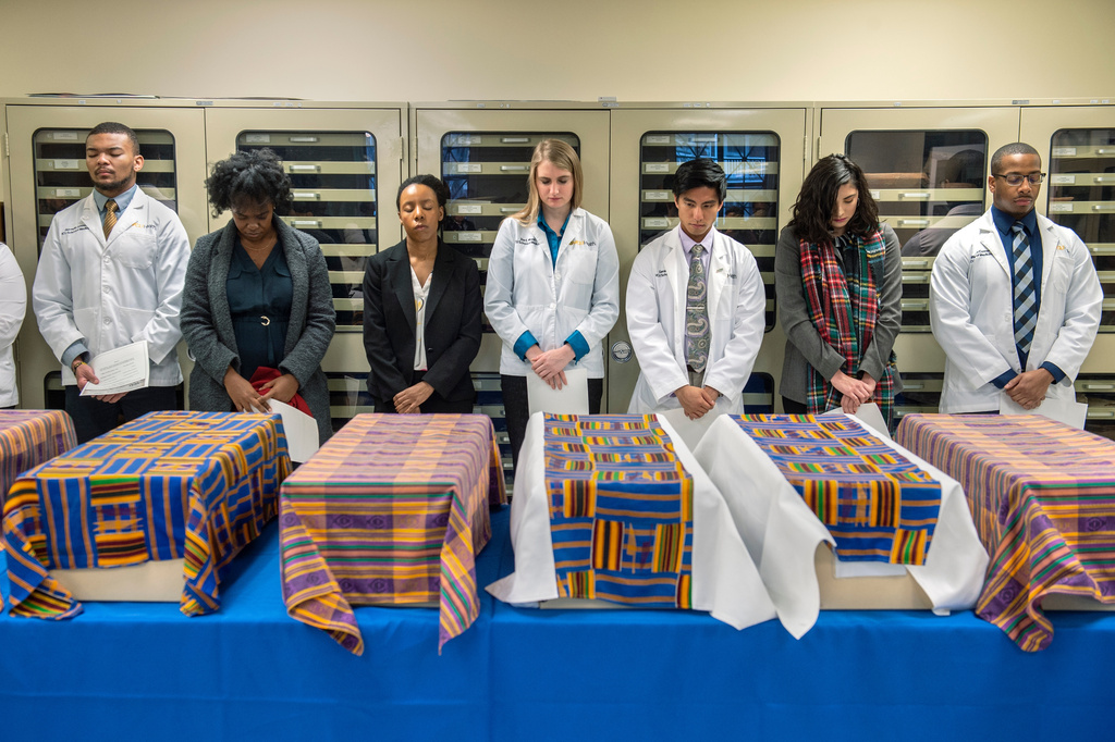 In this photo provided by Virginia Commonwealth University, people attend a memorial service standing behind caskets containing the remains of dozens of people whose remains were found in an abandoned well on the campus of VCU in Richmond, Va., in 2019. (VCU via AP)