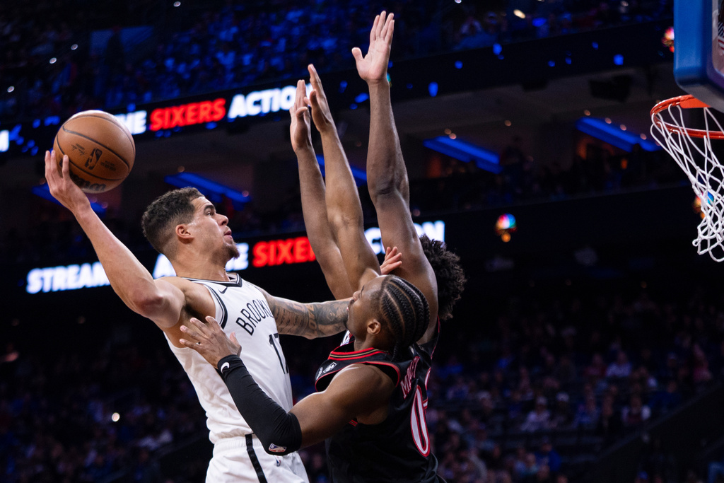 Brooklyn Nets' Michael Porter Jr., left, shots the ball against Philadelphia 76ers' Tyrese Maxey, center and Joel Embiid, right, during the first half of an NBA basketball game, Tuesday, Dec. 23, 2025, in Philadelphia. (AP Photo/Chris Szagola)