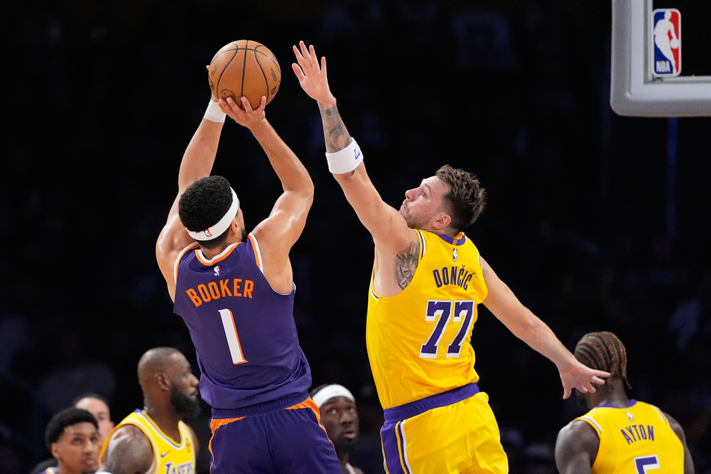 Phoenix Suns guard Devin Booker, left, shoots as Los Angeles Lakers guard Luka Doncic defends during the first half of an NBA basketball game Monday, Dec. 1, 2025, in Los Angeles. (AP Photo/Mark J. Terrill)
