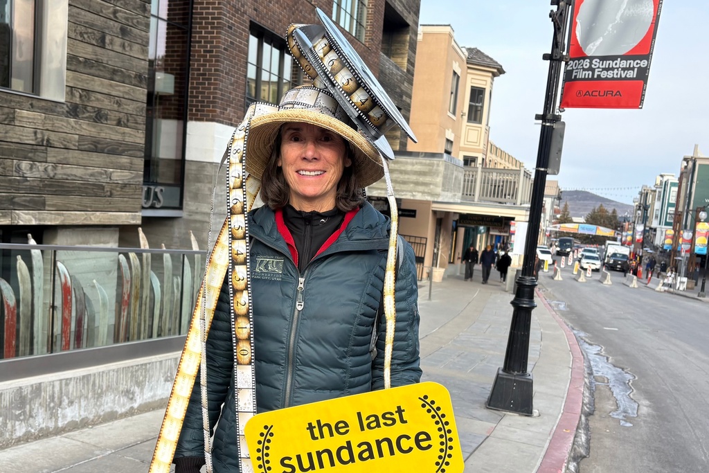 A woman wearing a film reel on her head holds a sign that reads "the last sundance" while attending final Sundance Film Festival in Park City, Utah, on Friday, Jan. 23, 2026, before the festival moves next year to Boulder, Colo. (AP Photo/Hannah Schoenbaum)