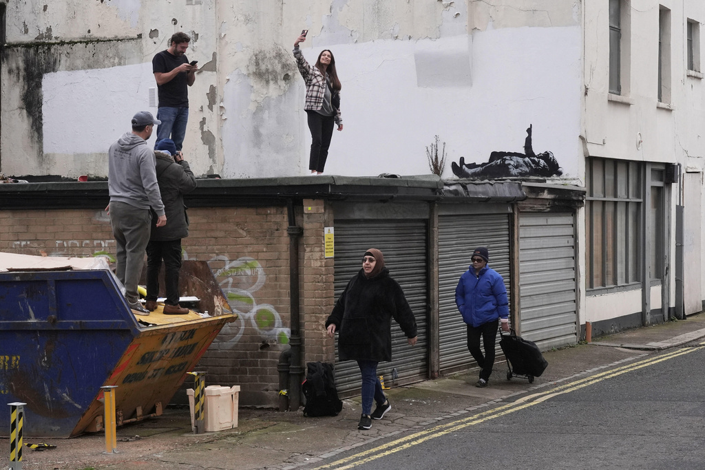 A person takes a selfie with a piece of graffiti artwork depicting two children, in London, Monday, Dec. 22, 2025 as elusive street artist Banksy appeared to confirm Monday that a new mural in London, depicting two children lying down and pointing up at the sky, is his latest work. (Stefan Rousseau/PA via AP)