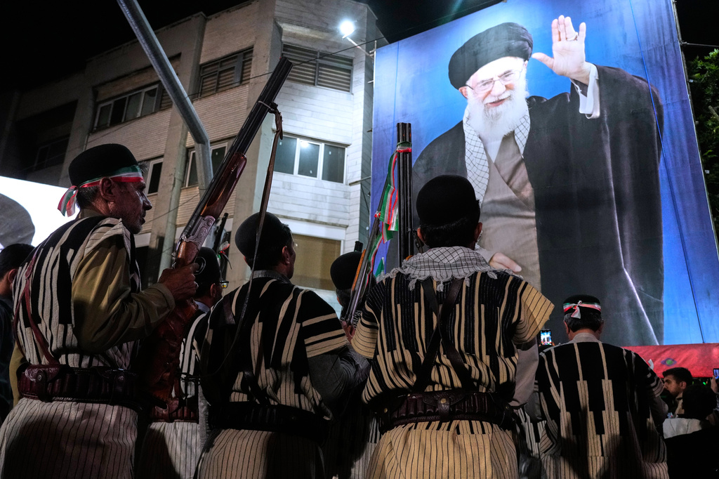 Bakhtiari nomads, wearing traditional dress, hold their guns during a pro-government gathering near the residence where former Iranian Supreme Leader Ayatollah Ali Khamenei, shown on a banner, was killed in U.S. and Israeli strikes on Feb. 28, in Tehran, Iran, Monday, May 18, 2026. (AP Photo/Vahid Salemi)