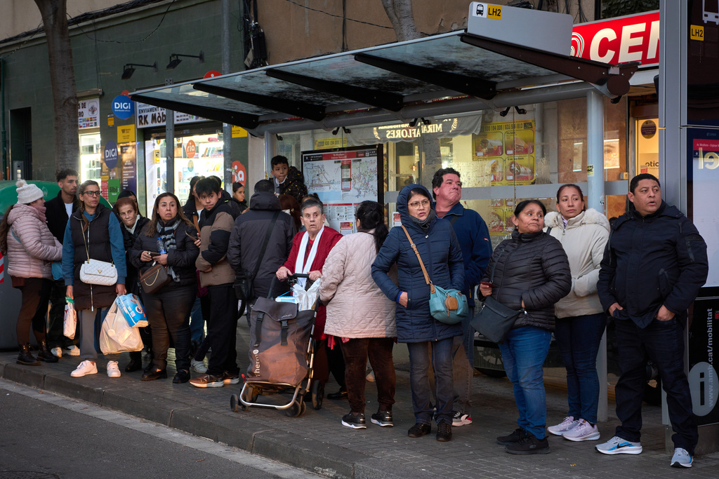 People from several Latin American countries, including Colombia, Peru and the Dominican Republic, along with Spaniards, wait at a bus stop in L'Hospitalet de Llobregat, near Barcelona, Spain, Friday, Jan. 30, 2026. (AP Photo/Emilio Morenatti)